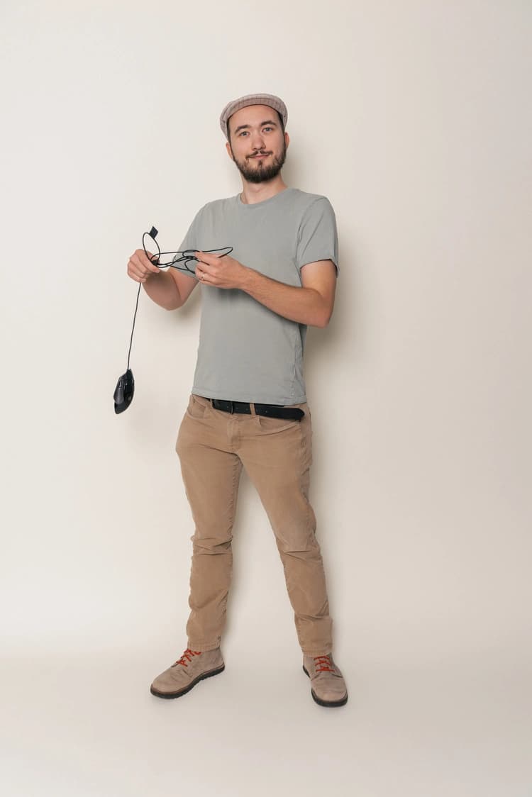 A person holding a computer mouse. The cable is heavily tangled up. The person looks surprised into the camera.